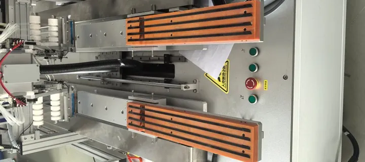 Dual-Head Tape Applicator with Magnetic Unloading — Parts on the fixtures with several tape strips applied at once (inside the machine)